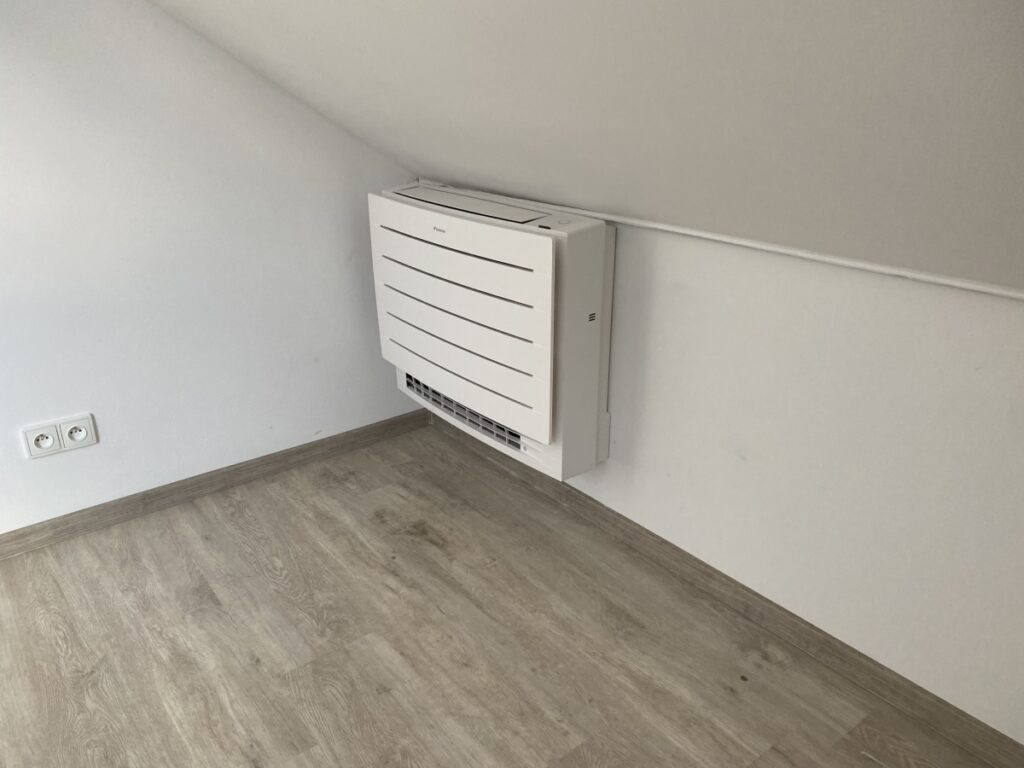 Bílá vnitřní klimatizační jednotka umístěná nízko na stěně