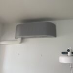 Šedá nástěnná klimatizační jednotka s instalační lištou v interiéru